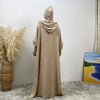 Une abaya beige avec capuche et manches batwing présentée sur un mannequin contre un mur blanc.