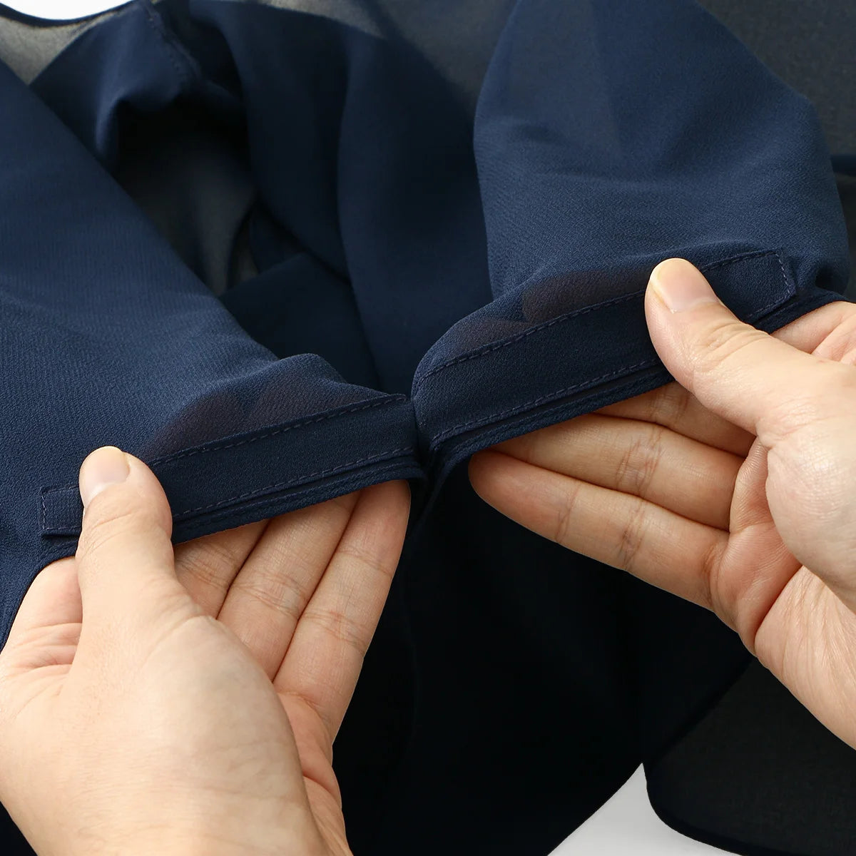 Manos ajustando un pañuelo de chifón azul oscuro con hebilla magnética