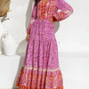 A woman models a long-sleeved, tiered maxi dress in pink with floral embroidery and lantern sleeves.