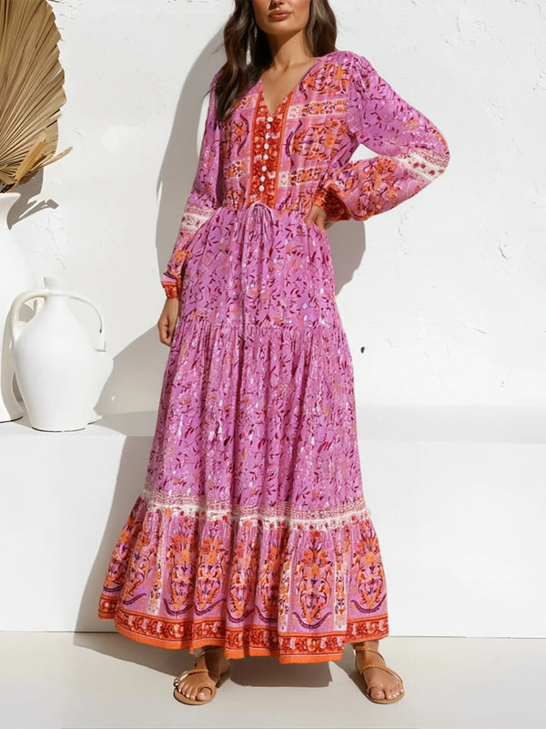 A woman models a long-sleeved, tiered maxi dress in pink with floral embroidery and lantern sleeves.