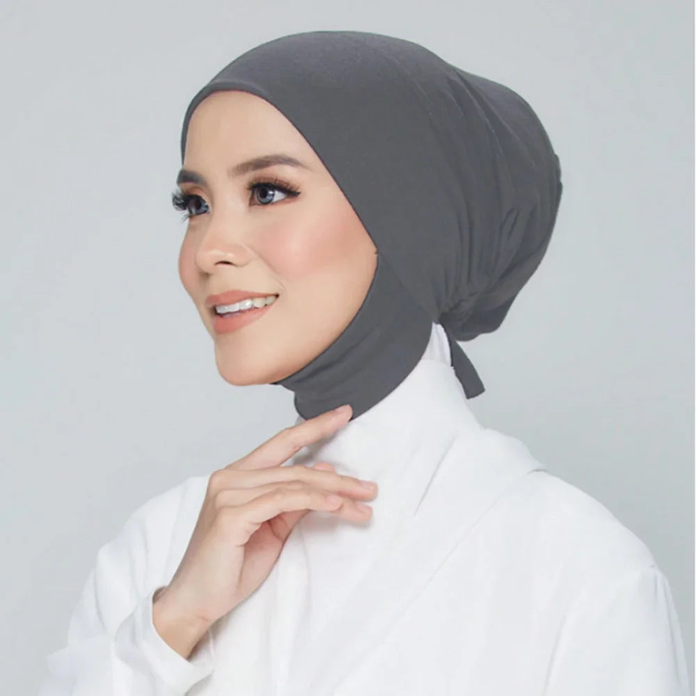 Une femme portant un foulard hijab gris uni et des vêtements blancs, souriant légèrement.
