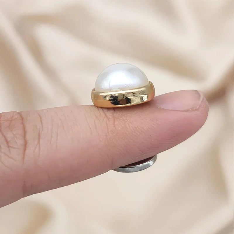 A gold-toned brooch featuring a smooth, round white pearl, designed for hijab clips.