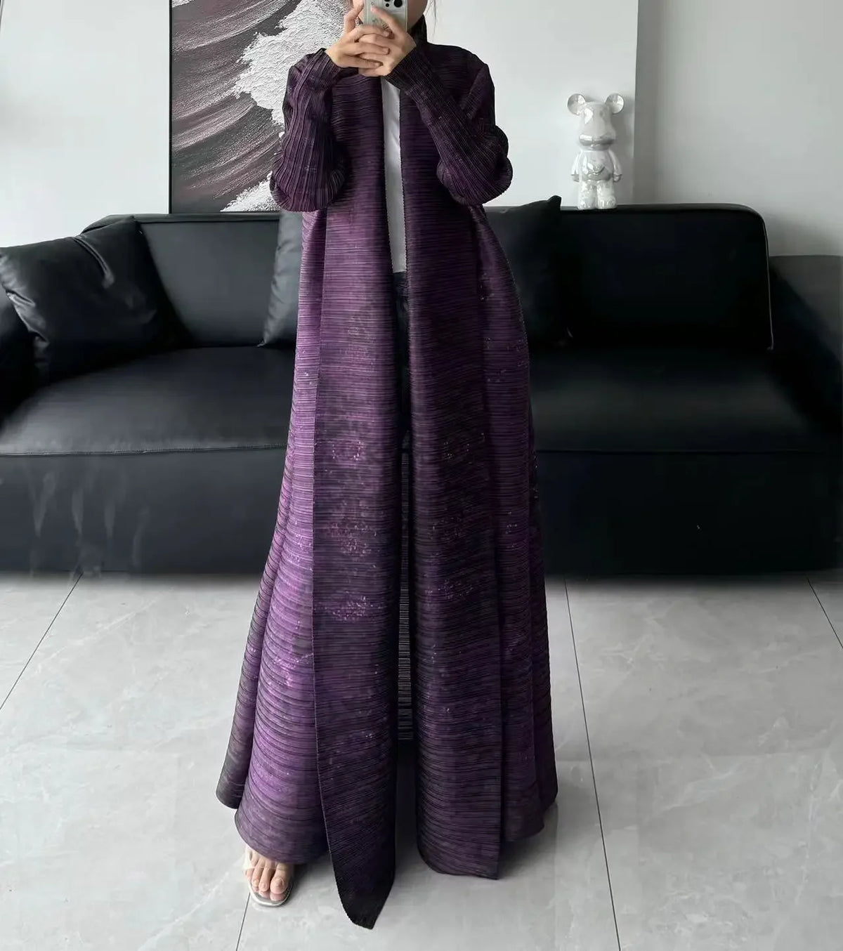 Une personne modélise une veste coupe-vent plissée longue et violette en plan complet.
