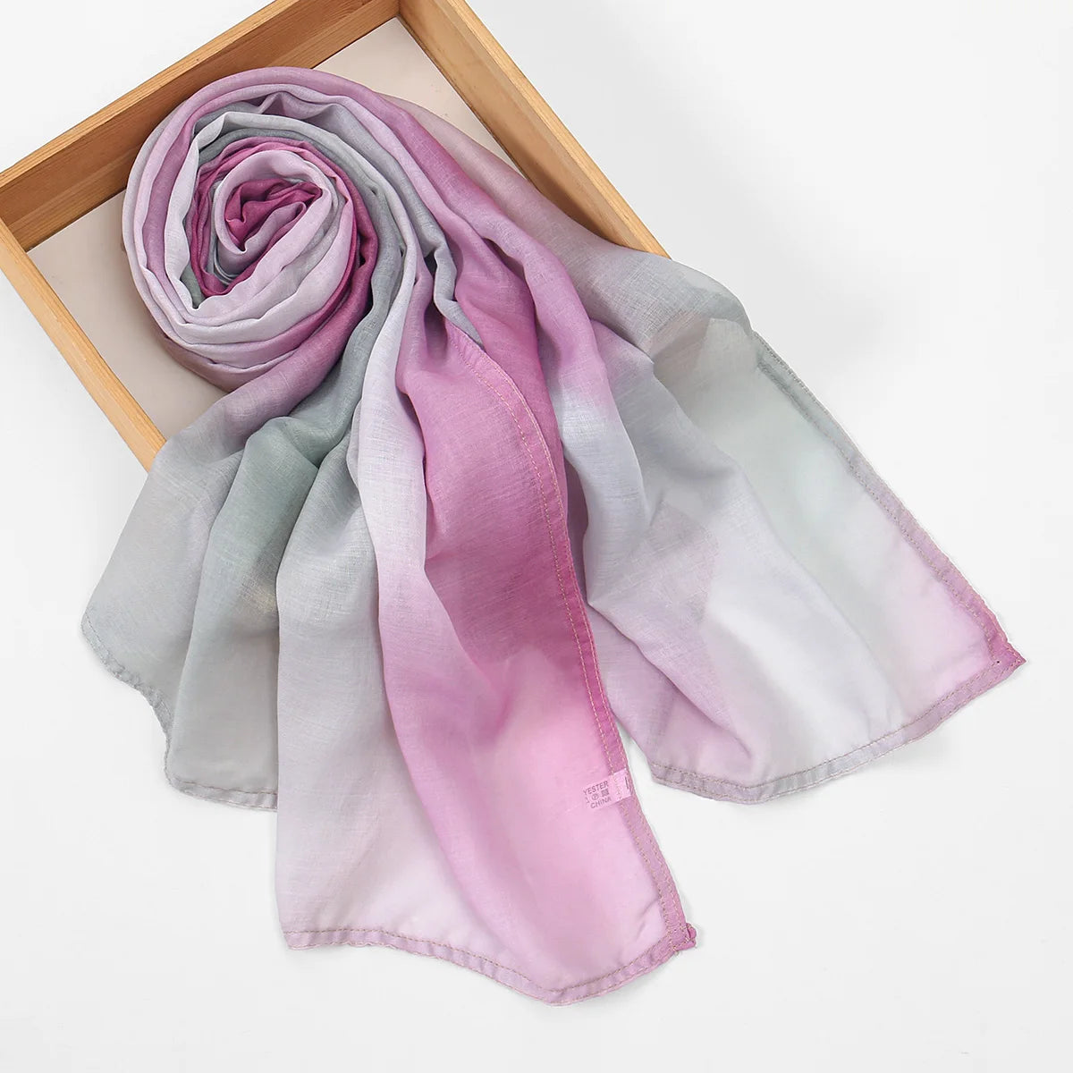 Un foulard de coton à imprimé floral, doux et fluide, dans des tons de lavande et de rose, drapé sur un cadre en bois.