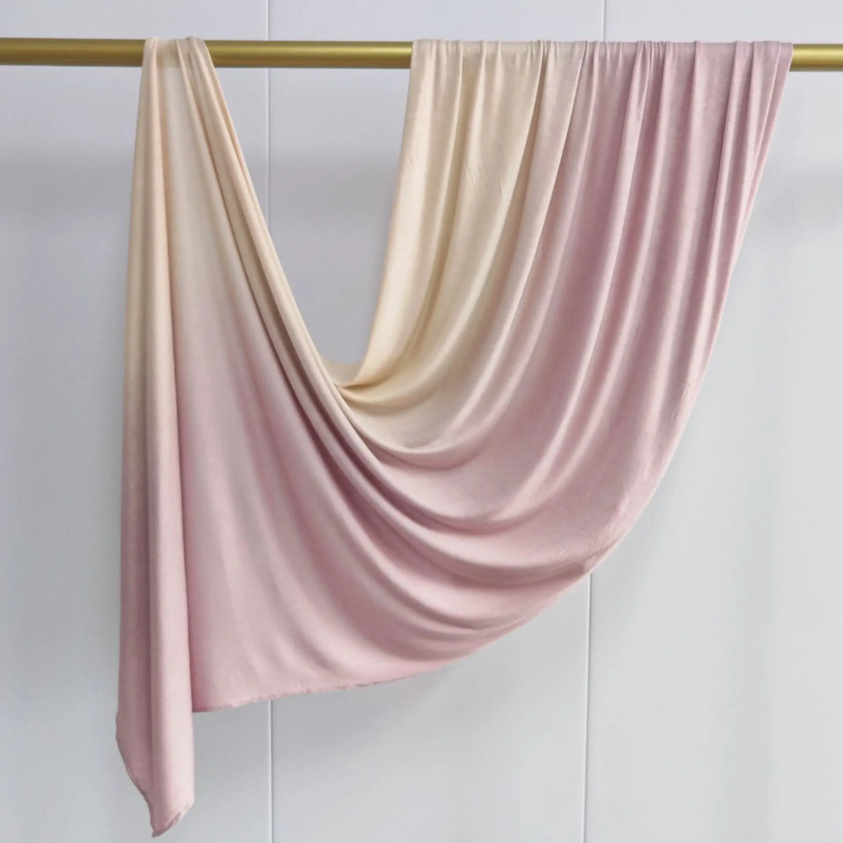Pañuelo de algodón rosa suave de doble cara con degradado, colgado en una percha de madera.