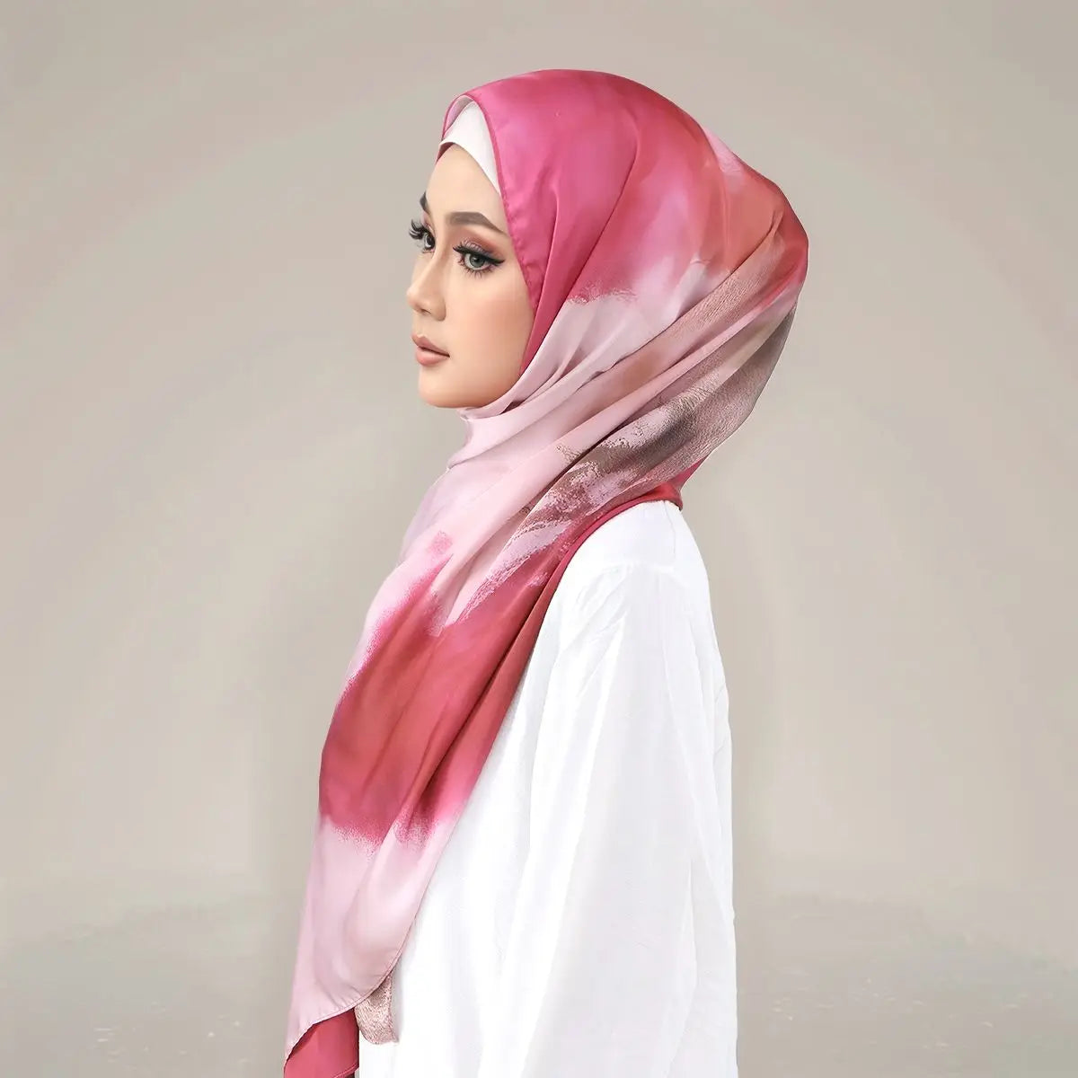 Eine Frau trägt einen rosa-weißen bedruckten Seidenschal als Hijab über ein weißes Kleidungsstück.