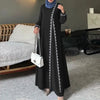 Eine Frau in einem eleganten schwarzen Abaya-Kleid mit weißer Spitze und einer weißen Handtasche.