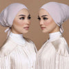 Una mujer vistiendo un elegante turbante modal rosa claro y una blusa de satén a juego.