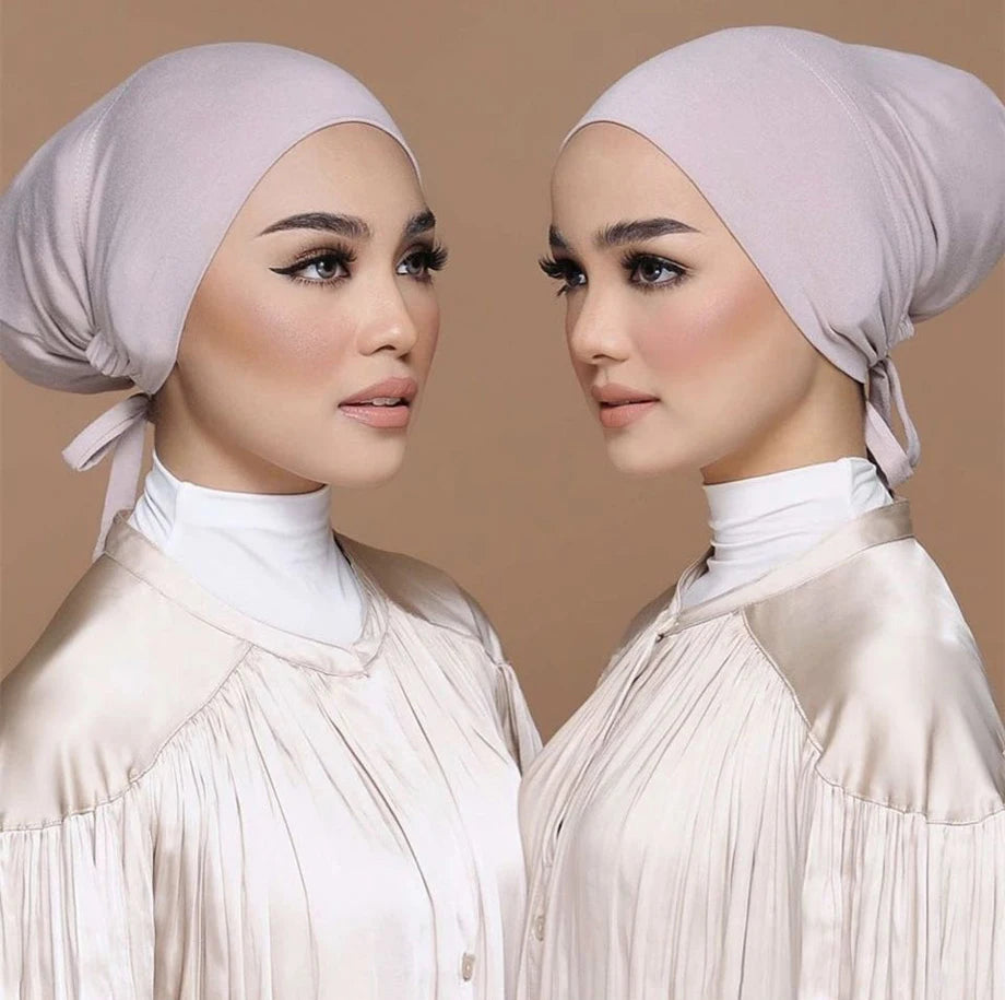 Una mujer vistiendo un elegante turbante modal rosa claro y una blusa de satén a juego.