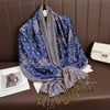Una pashmina de seda azul profunda con bordado y flecos dorados, drapeada sobre un sofá de cuero marrón.