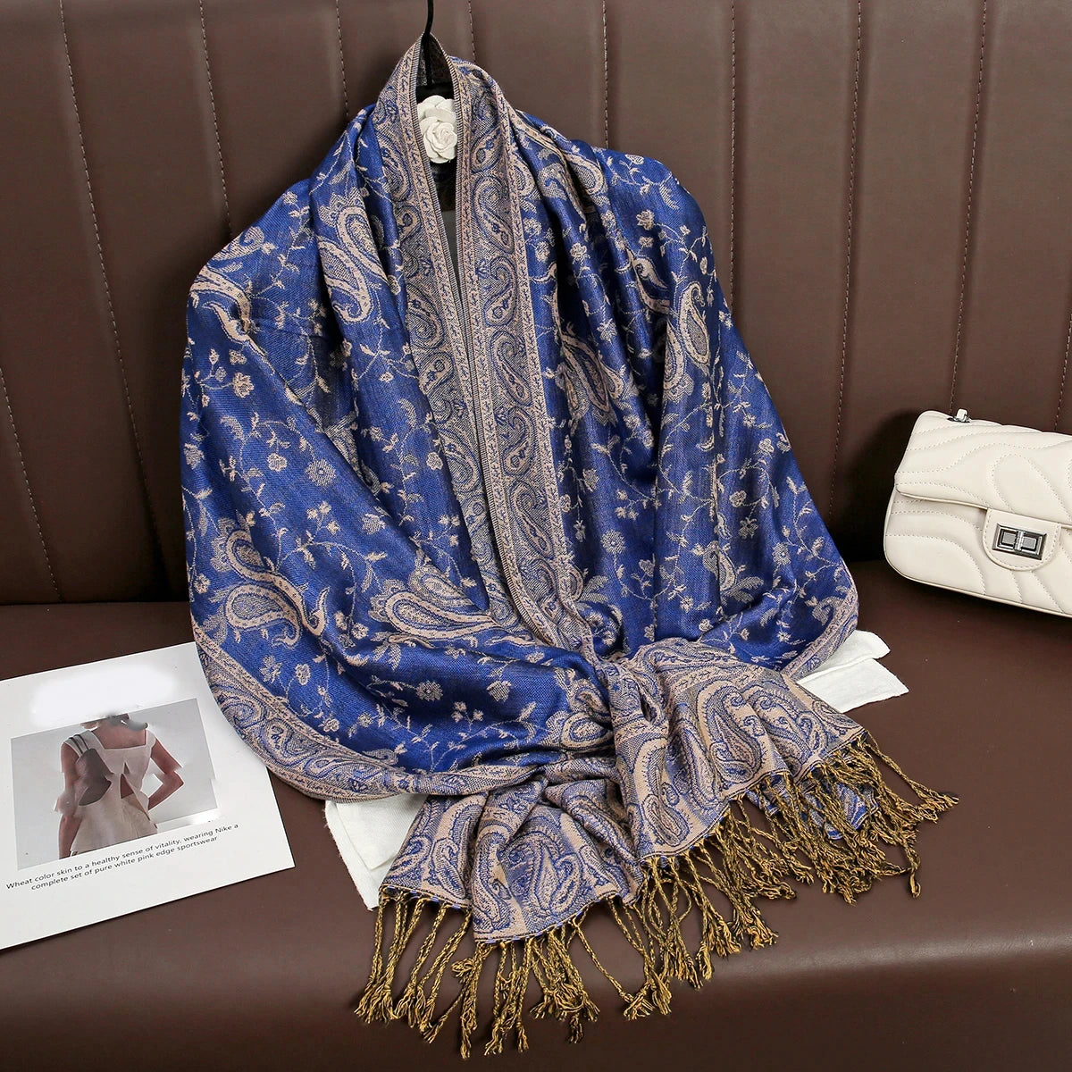 Una pashmina de seda azul profunda con bordado y flecos dorados, drapeada sobre un sofá de cuero marrón.