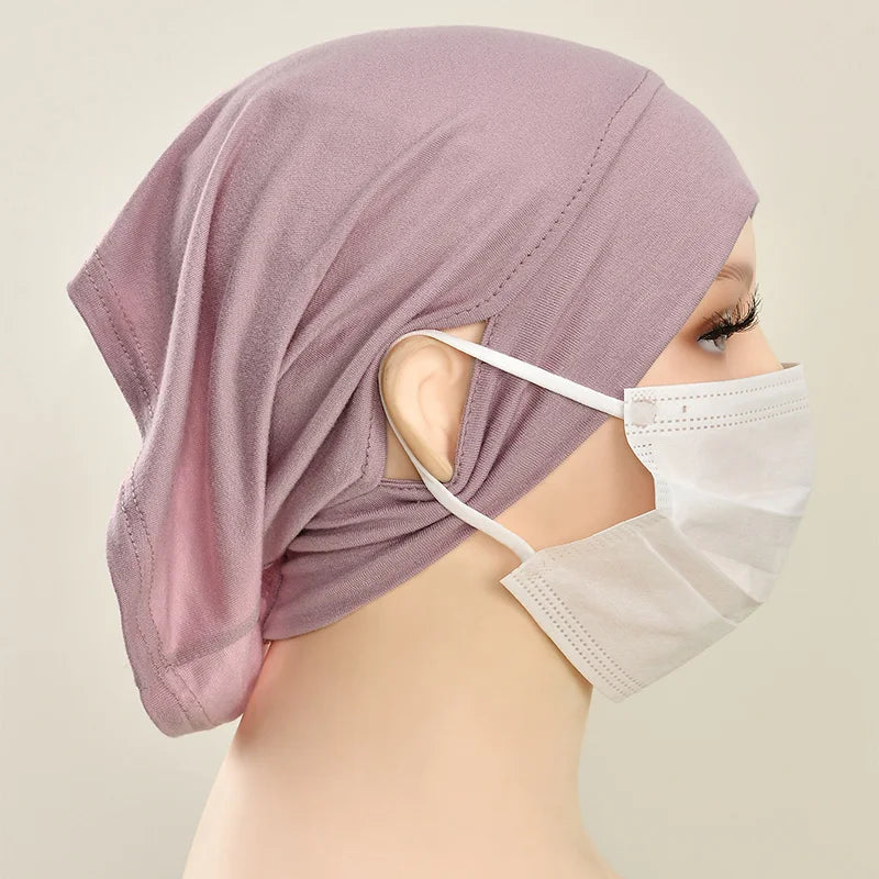 Eine Frau trägt eine staubrosa Jersey-Baumwoll-Hijabkappe und eine weiße Schutzmaske.
