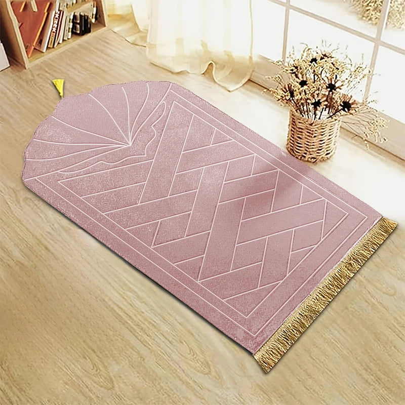 Alfombra de oración rosa grabada con patrón geométrico y borlas doradas sobre un suelo de madera clara.