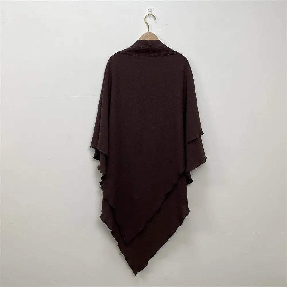 A dark brown two-layer everyday hijab scarf draped on a hanger against a white wall.