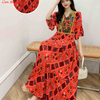 Eine Frau modelliert ein leuchtend rotes, bohemiss-besticktes Maxi-Kleid mit farbenfrohen Mustern und Ärmeln.