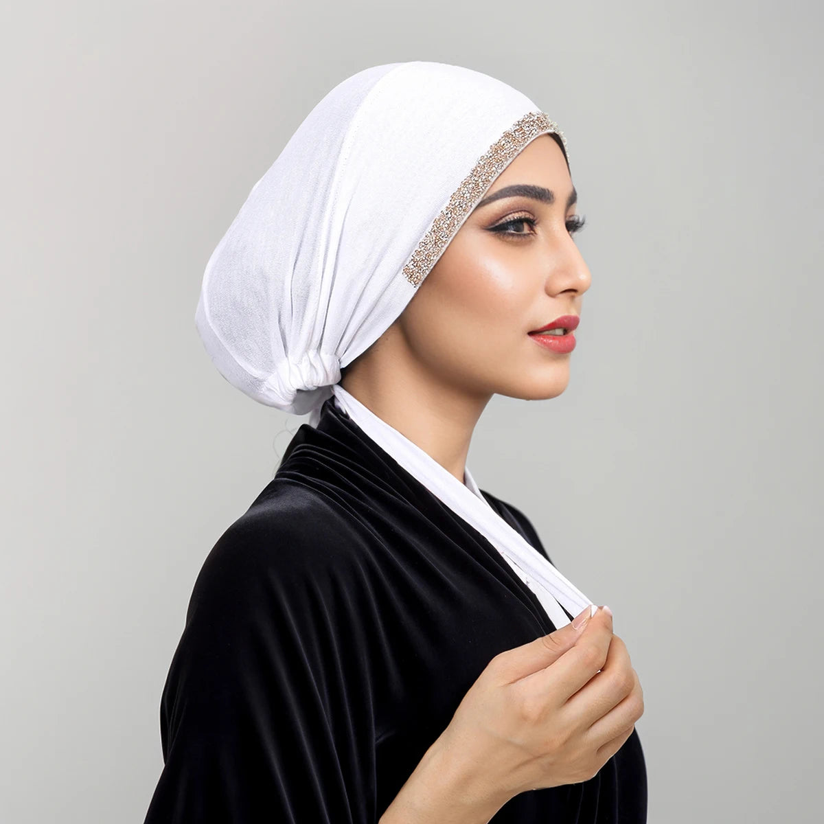Frau mit weißem Strass-Hijab und schwarzem Samtgewand, im Profil.
