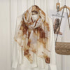 Pañuelo de algodón viscosa estampado beige y marrón drapeado alrededor de una blusa blanca, mostrado en una percha.