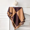 Pañuelo pashmina geométrico marrón y beige sobre una estantería blanca con un objeto de cerámica.