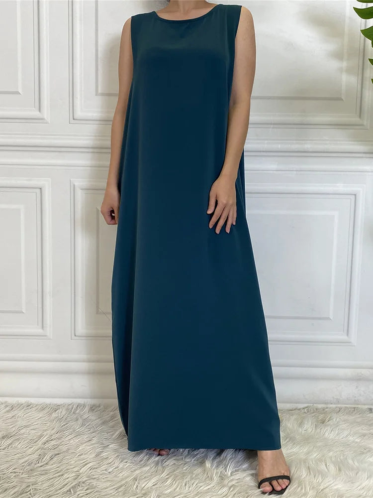 Eine Frau in einem eleganten, ärmellosen, dunkeltürkisen Kaftan-Kleid drinnen.
