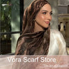A woman wearing a brown and beige watercolor print scarf draped over her head, looking to the side.