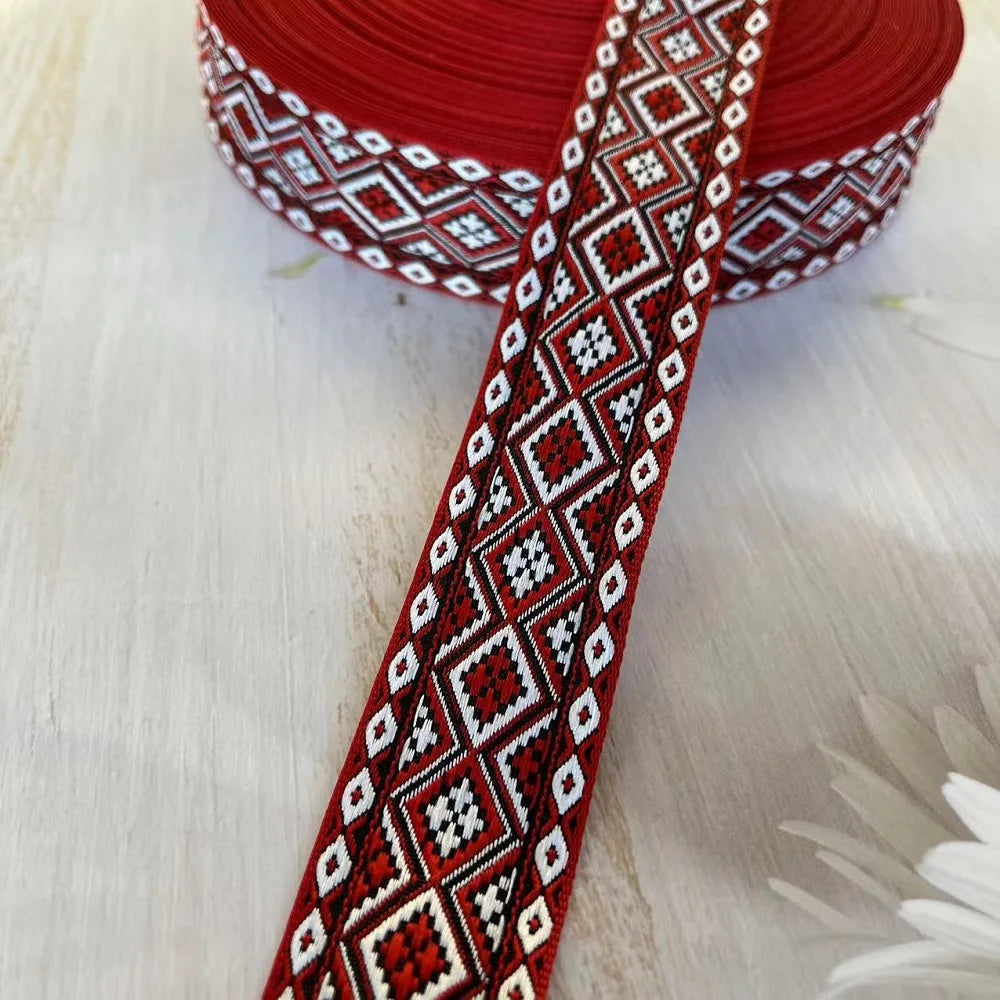 Primer plano de una cinta jacquard geométrica roja y blanca con patrón de diamantes repetitivo, enrollada en tela roja.