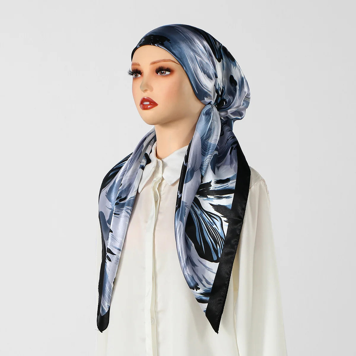 Eine Frau modelliert einen blau-schwarz gemusterten Seidenturban-Hijab-Schal um ihren Kopf.