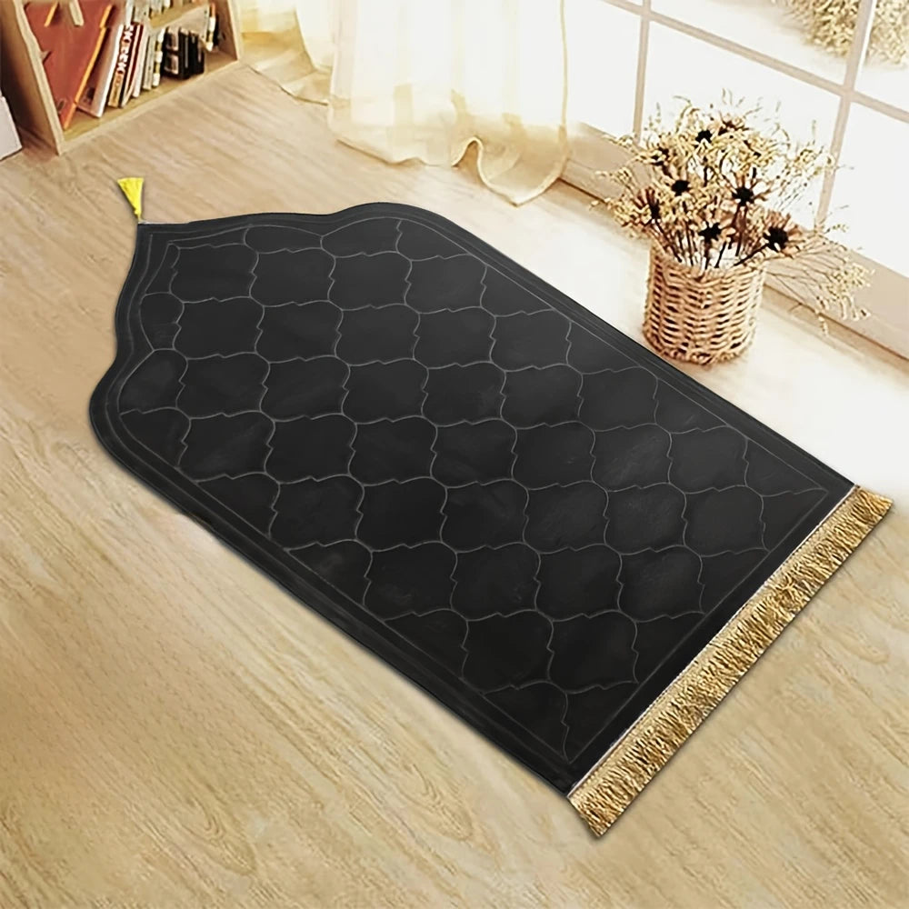 Tapis de prière noir embossé avec une pompon or sur un plancher en bois clair.
