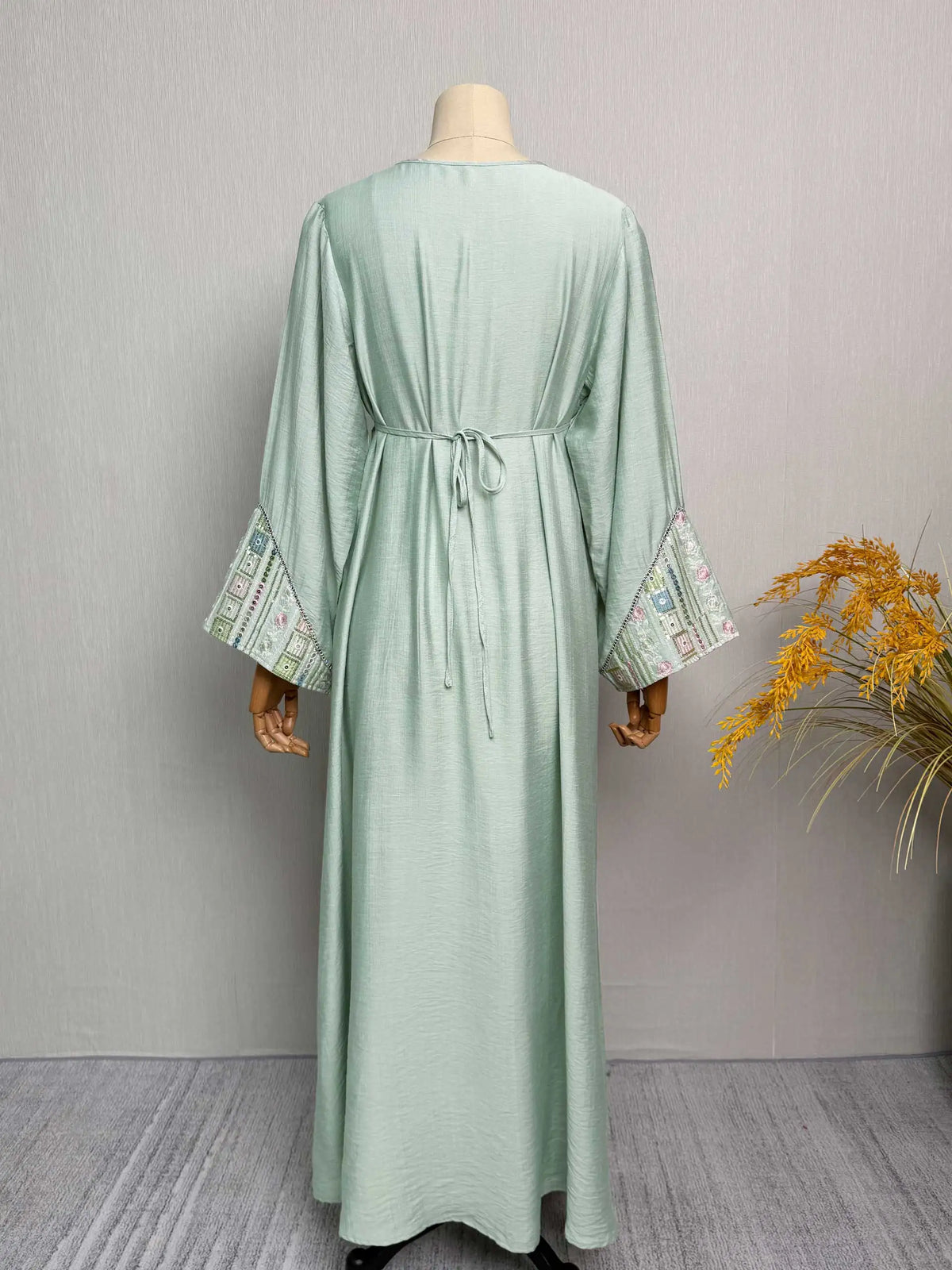Hellgrüne Abaya mit Paillettenstickerei und verzierten Ärmeln auf einem Mannequin.