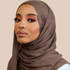 Une femme portant un châle en crinkle de rayon marron drapé sur sa tête et ses épaules.