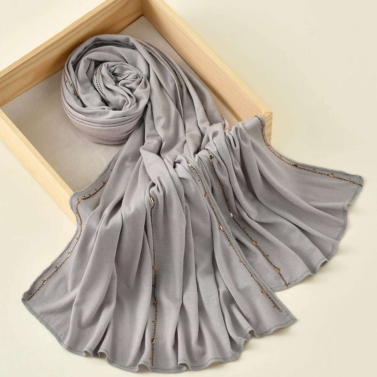 Pañuelo de jersey de algodón con brillo plateado gris suave, enrollado y drapeado en una caja de madera.