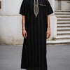 A man wearing a black striped Moroccan ethnic thobe with a stand collar and gold embroidery, standing outdoors.