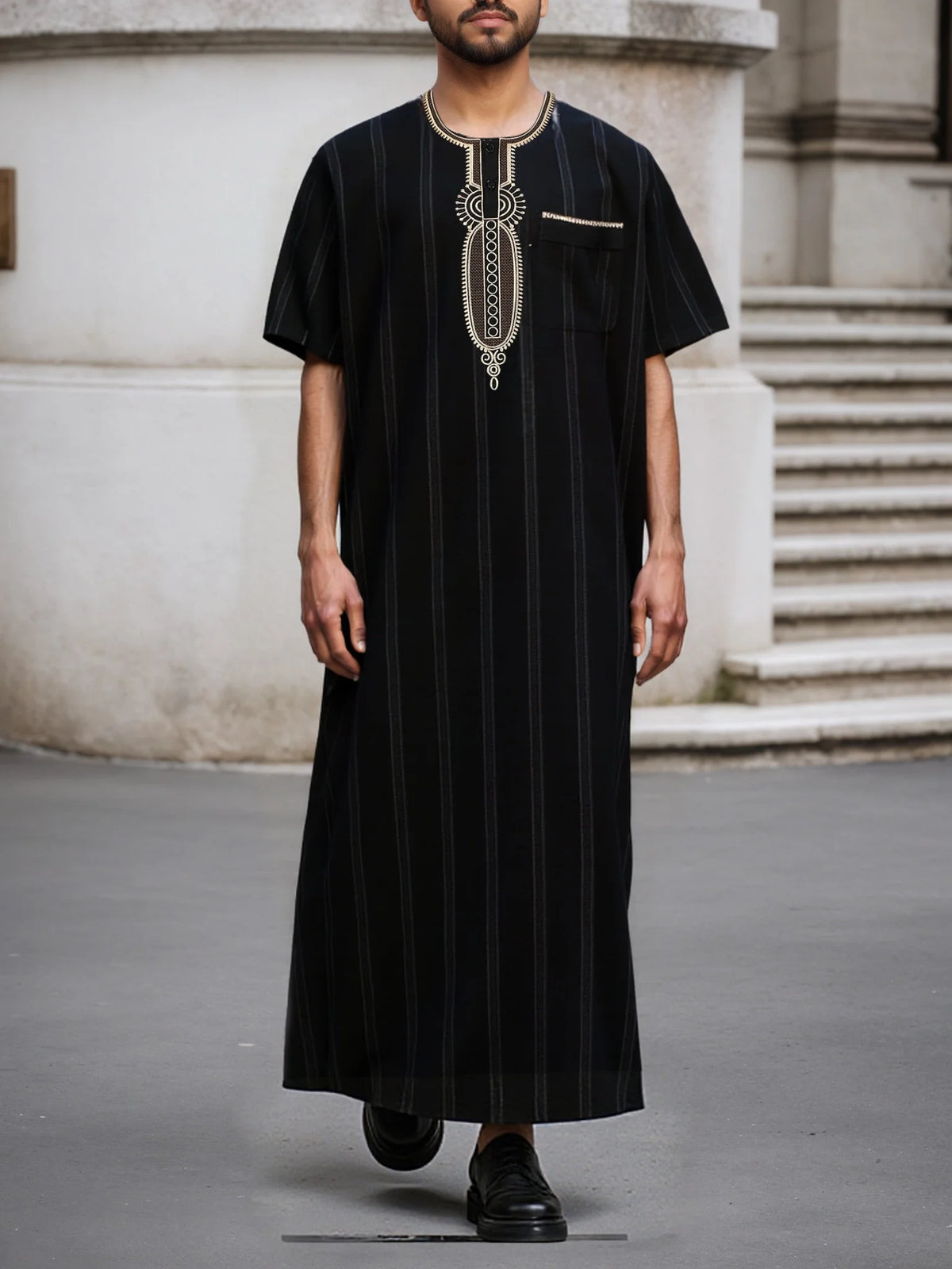 A man wearing a black striped Moroccan ethnic thobe with a stand collar and gold embroidery, standing outdoors.