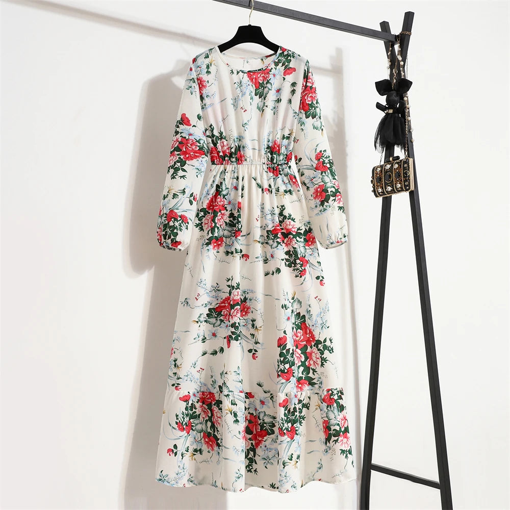 Weißes Maxi-Kleid mit Blumenmuster in roten und grünen Rosen, an einem schwarzen Kleiderständer hängend.