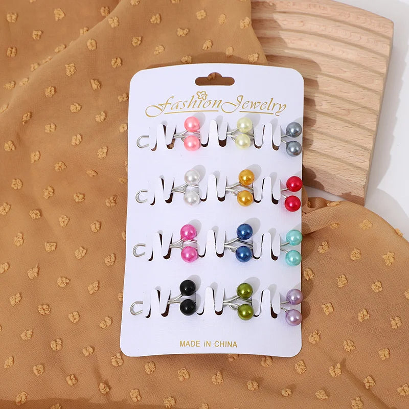 Un ensemble de pinces et épingles à hijab en strass argentés présentées sur une carte blanche sur un fond de tissu beige.