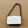 Bolso de cuero acolchado blanco con correa de cadena plateada, exhibido sobre una superficie marrón.