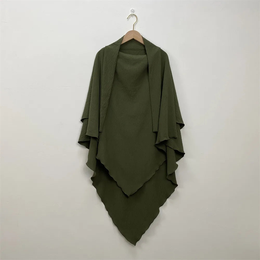 A dark olive green two-layer everyday hijab scarf draped on a hanger against a light wall.