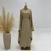 Beige, elegante, langärmelige Abaya mit goldfarbener Halskette auf einem Mannequin.