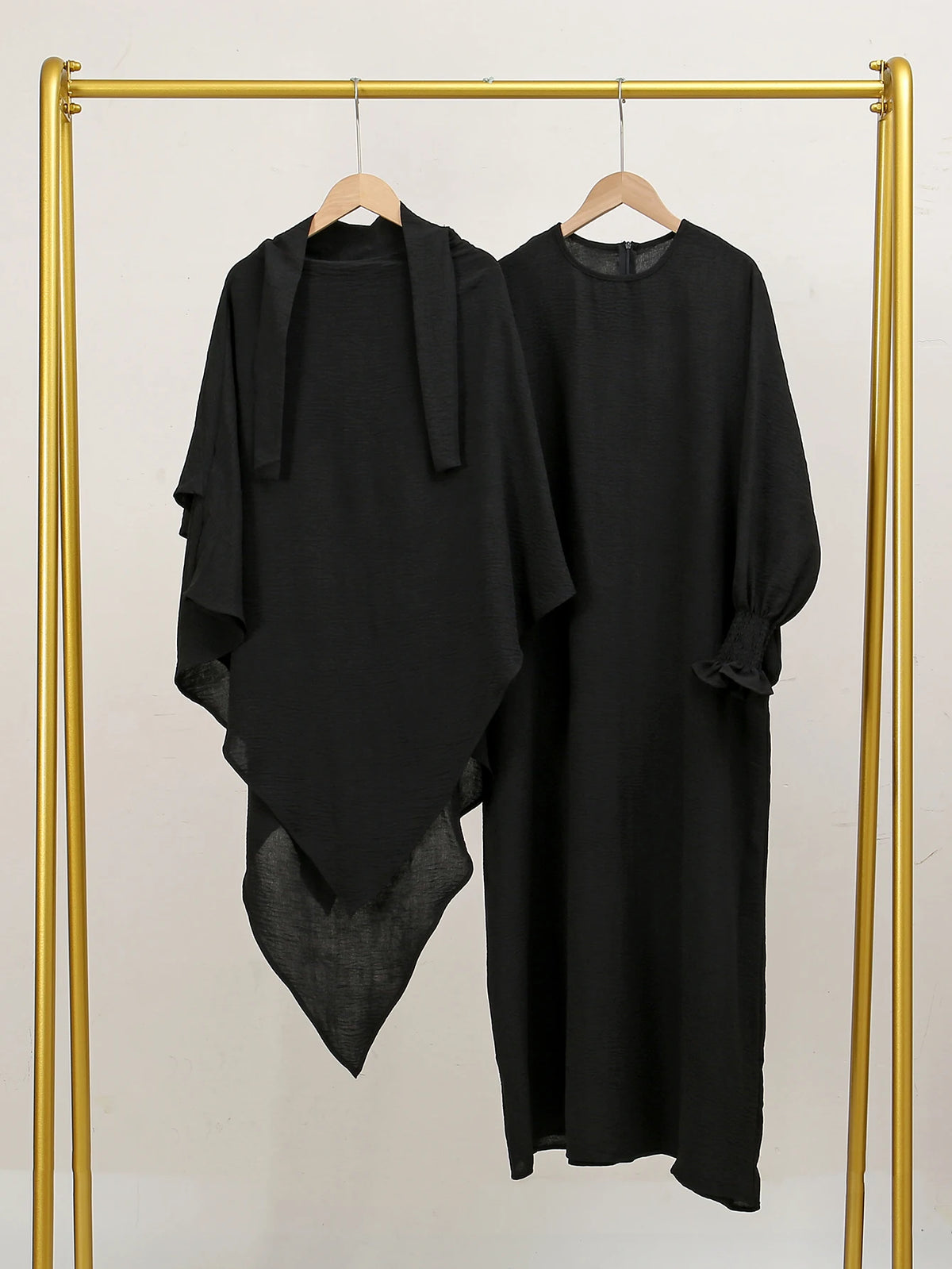 Elegante schwarze Abaya und Khimar-Set auf goldener Kleiderstange vor hellem Hintergrund.