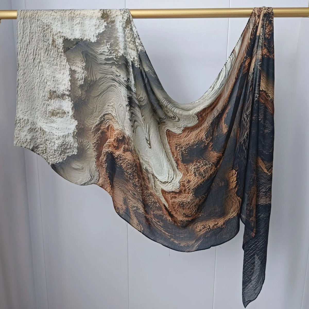 Drapierter, mehrfarbiger Hijab-Schal mit abstrakten Texturen und erdigen Tönen, aufgehängt an einem Holzstab.