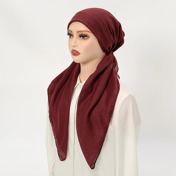 A model wearing a solid maroon linen hijab cap and scarf with a white top.