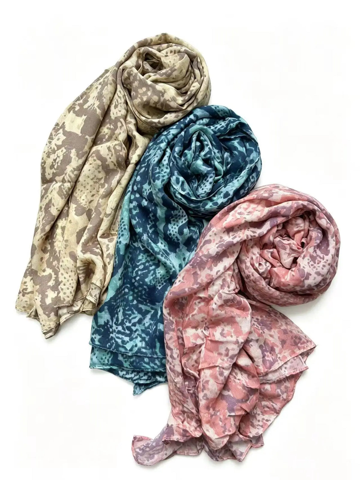 Drei gerollte, mehrfarbige Hijab-Schals in Beige-, Türkis- und Rosa-Tönen.