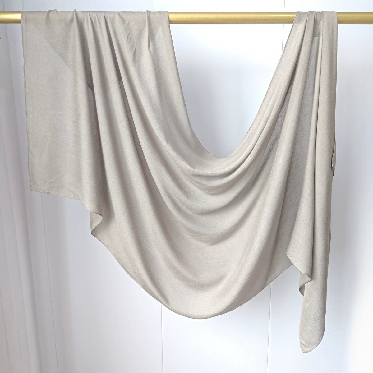 Foulard hijab uni beige clair drapé sur un cintre doré.