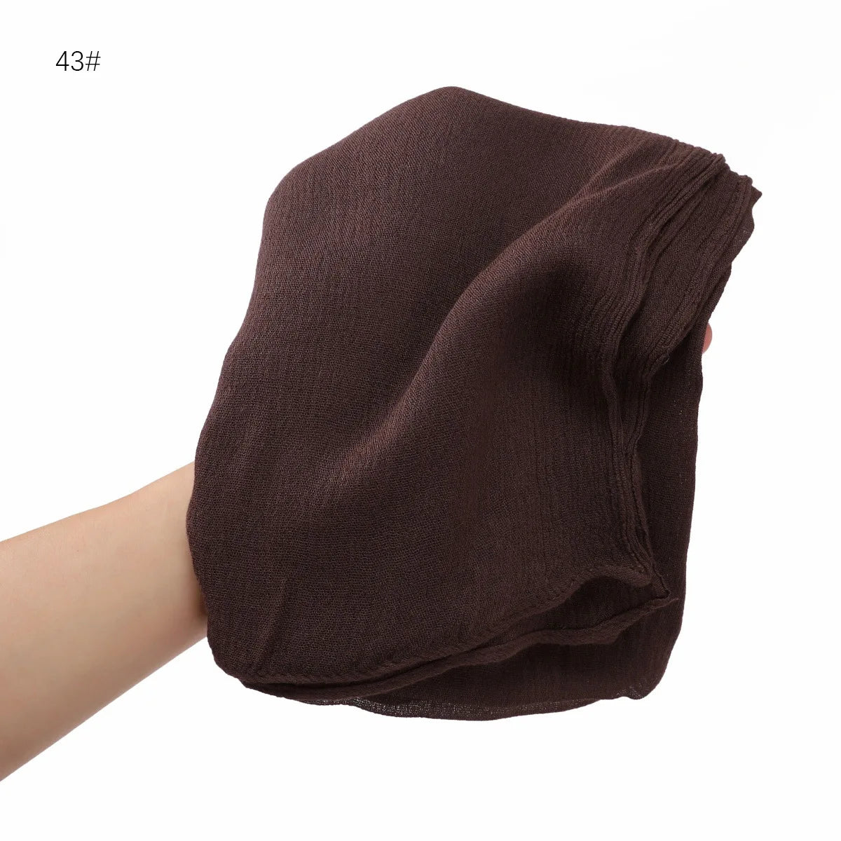 Écharpe châle crinkle en rayon brun foncé pliée et tenue par une main.