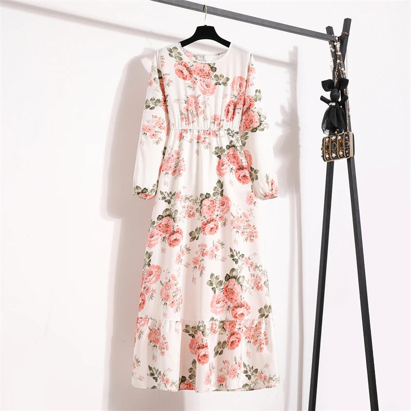 Weißes Maxi-Kleid mit Blumenmuster aus rosa und grünen Rosen, an einem schwarzen Haken hängt.