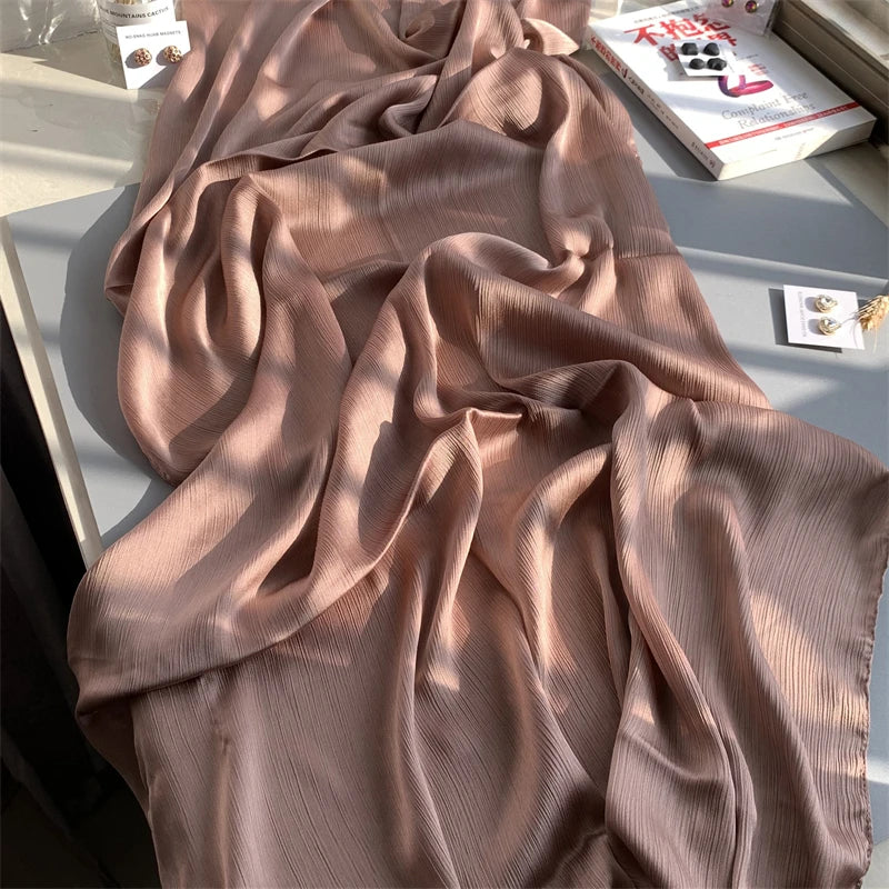 Ein drapierter Stoff aus staubrosa crinkligem Satin-Chiffon wird neben einer Box präsentiert.