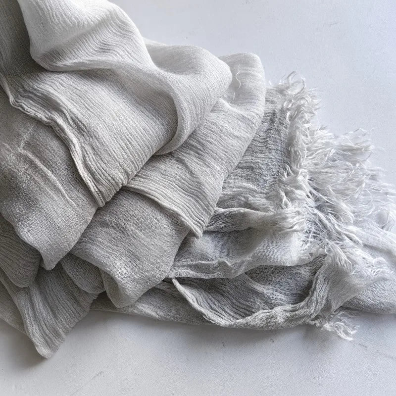 Une pile de foulards de hijab en viscose coton doux gris clair avec pompons.