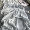 Weißes gerüschtes Satin-Chiffon-Hijab-Stoff, drapiert auf einer grauen Oberfläche neben einem Buch.