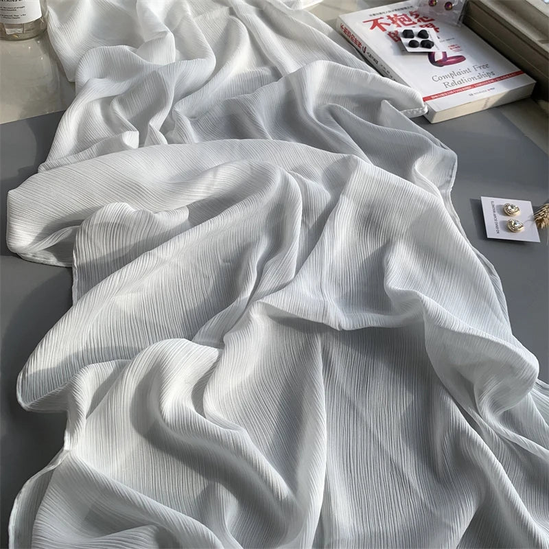 Weißes gerüschtes Satin-Chiffon-Hijab-Stoff, drapiert auf einer grauen Oberfläche neben einem Buch.
