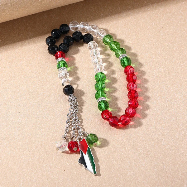 A bracelet made of prayer beads featuring black, white, and green stones with a Palestinian flag charm.