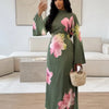 Eine Frau modelliert ein elegantes, langärmeliges olivgrünes Abaya-Kleid mit rosa Blumenprint in einem hellen Wohnzimmer.